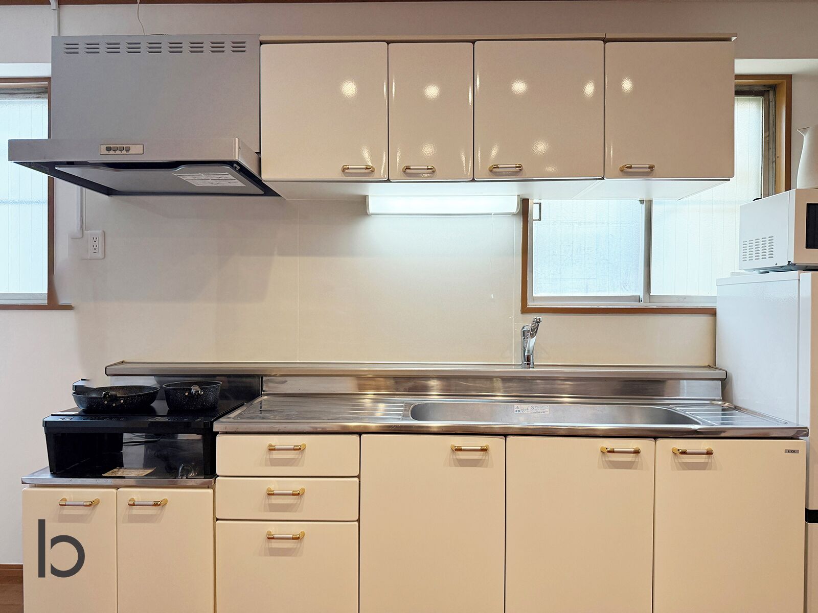 A kitchen with a stainless steel sink, a stove, and beige cabinets with gold handles.