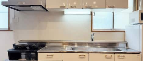 A kitchen with a stainless steel sink, a stove, and beige cabinets with gold handles.
