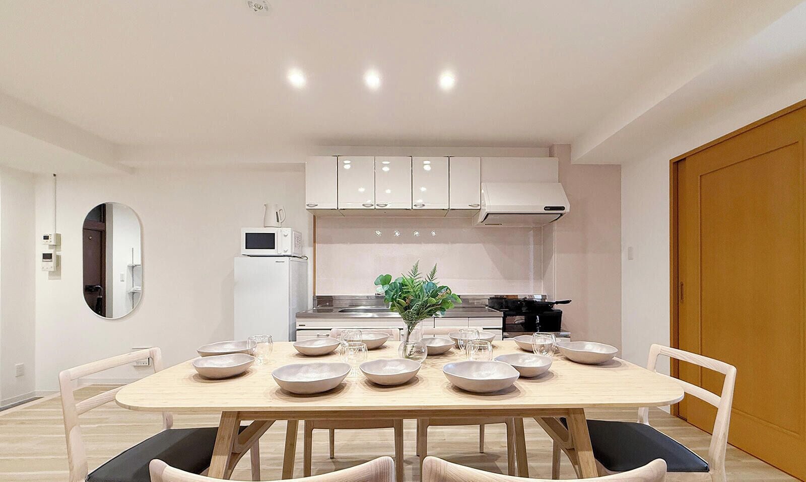 A modern kitchen with white cabinets, a dining table set with bowls and glasses, and a potted plant.