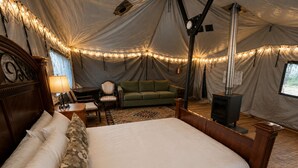 A tented accommodation with a bed, a sofa, a table, and a fireplace.