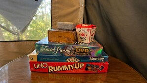 A stack of board games on a table near a window with a view of trees.