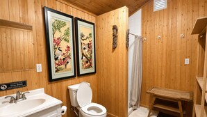 A bathroom with wooden paneling, a toilet, a sink, and two framed artworks.