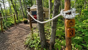 Une zone boisée, délimitée par une barrière en corde, avec un poteau en bois portant le numéro de l’emplacement et une tente en arrière-plan.