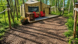 Une tente avec une table et deux chaises, entourée d’une forêt.