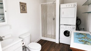 A bathroom with a toilet, sink, shower, and stacked washer and dryer.