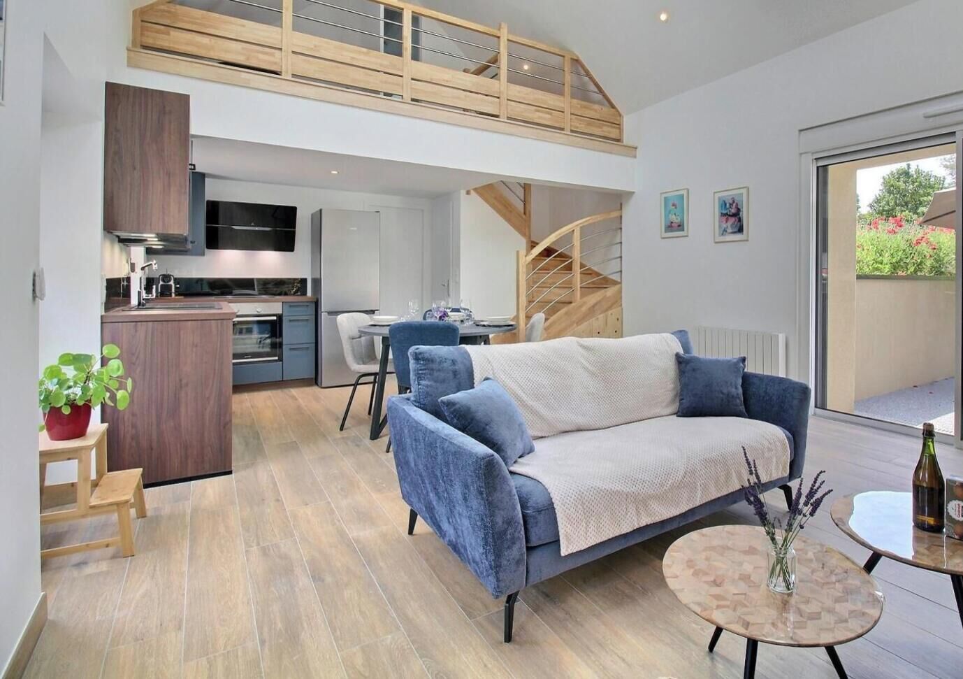 A modern interior with a sofa, a dining area, a kitchen, and a staircase leading to an upper level.