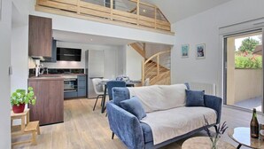 Um interior moderno com um sofá, sala de jantar, cozinha e escada que leva a um andar superior.