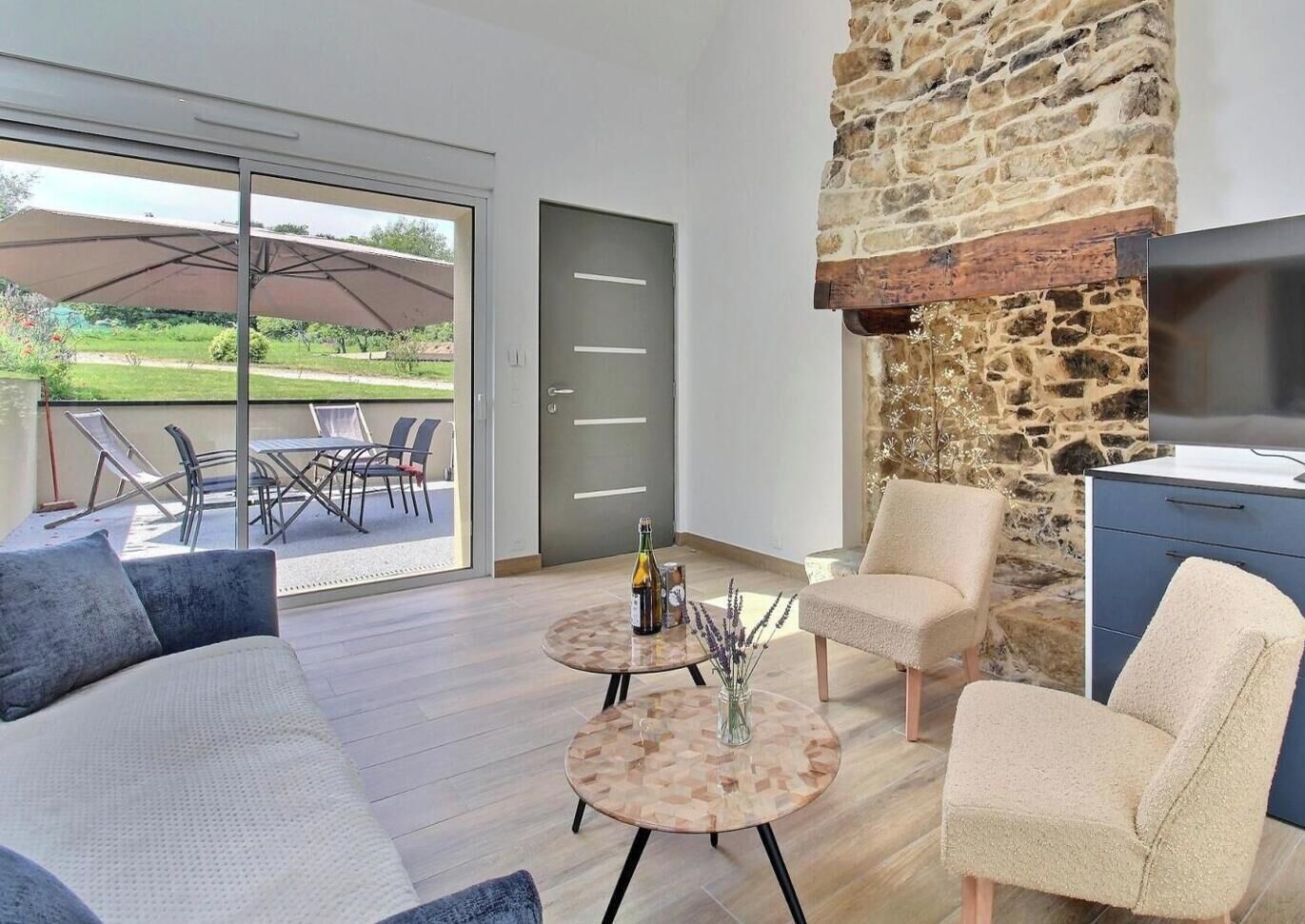 Ein modernes Wohnzimmer mit Kamin aus Stein, einer Couch, zwei Sesseln, einem Couchtisch und Blick auf die Außenpatio-Terrasse.