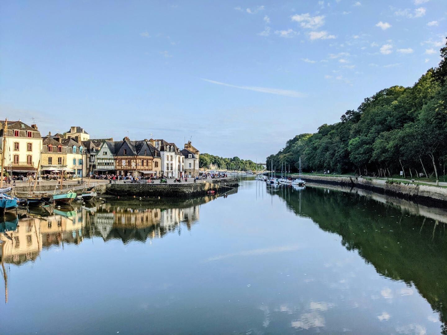 A calm river with boats, a waterfront promenade, and historic buildings along the riverbank.