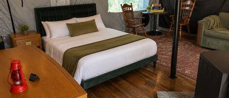 Een tentaccommodatie met een bed, zithoek en een tafel met een rode fles.