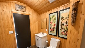 Un baño con paneles de madera, un inodoro blanco, un lavabo y dos cuadros en la pared.