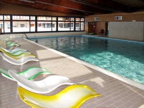 Ein hallenbad mit klarem Wasser, gefliestem Boden und einer Reihe bunter Liegestühle am Rand.