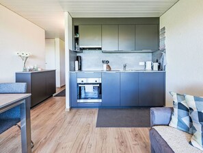 Eine kompakte Küche mit modernen Geräten, ein Essbereich mit Tisch und Stühlen sowie eine gemütliche Sitzecke mit Sofa und Kissen.
