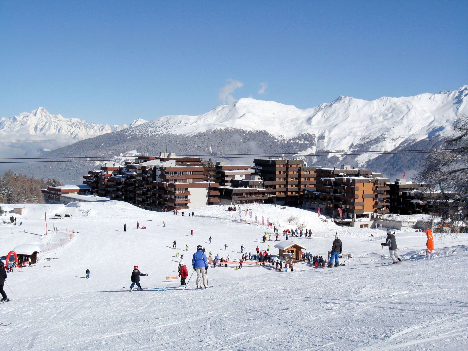Estância de esqui com vários edifícios, uma pista de esqui e montanhas cobertas de neve ao fundo.