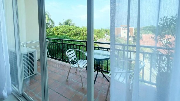 A balcony with a glass door, a white chair, a small round table, and a view of greenery and buildings.