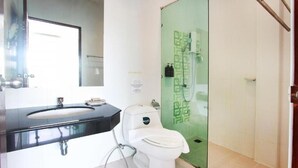 A bathroom with a glass shower enclosure, a white toilet, and a black sink with a mirror above it.