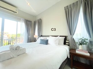 A hotel room with a large bed, a bedside table with a lamp, a window with curtains, and a view of the outdoors. - The Zen Suites (Rawai)