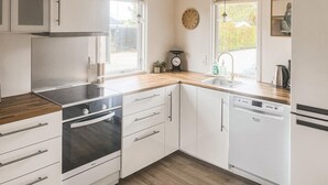 A modern kitchen with white cabinetry, a built-in oven, a dishwasher, and a window with a view of greenery. - Nice home in Assens with WiFi (Assens)