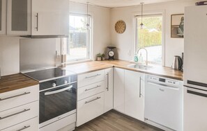 Eine moderne Küche mit weißen Schränken, einem Backofen, einem Geschirrspüler und einem Fenster mit Blick ins Grüne.