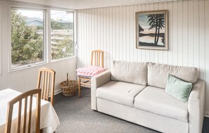 Een gezellige kamer met een bank, een stoel, een tafel en een raam met uitzicht op groen.