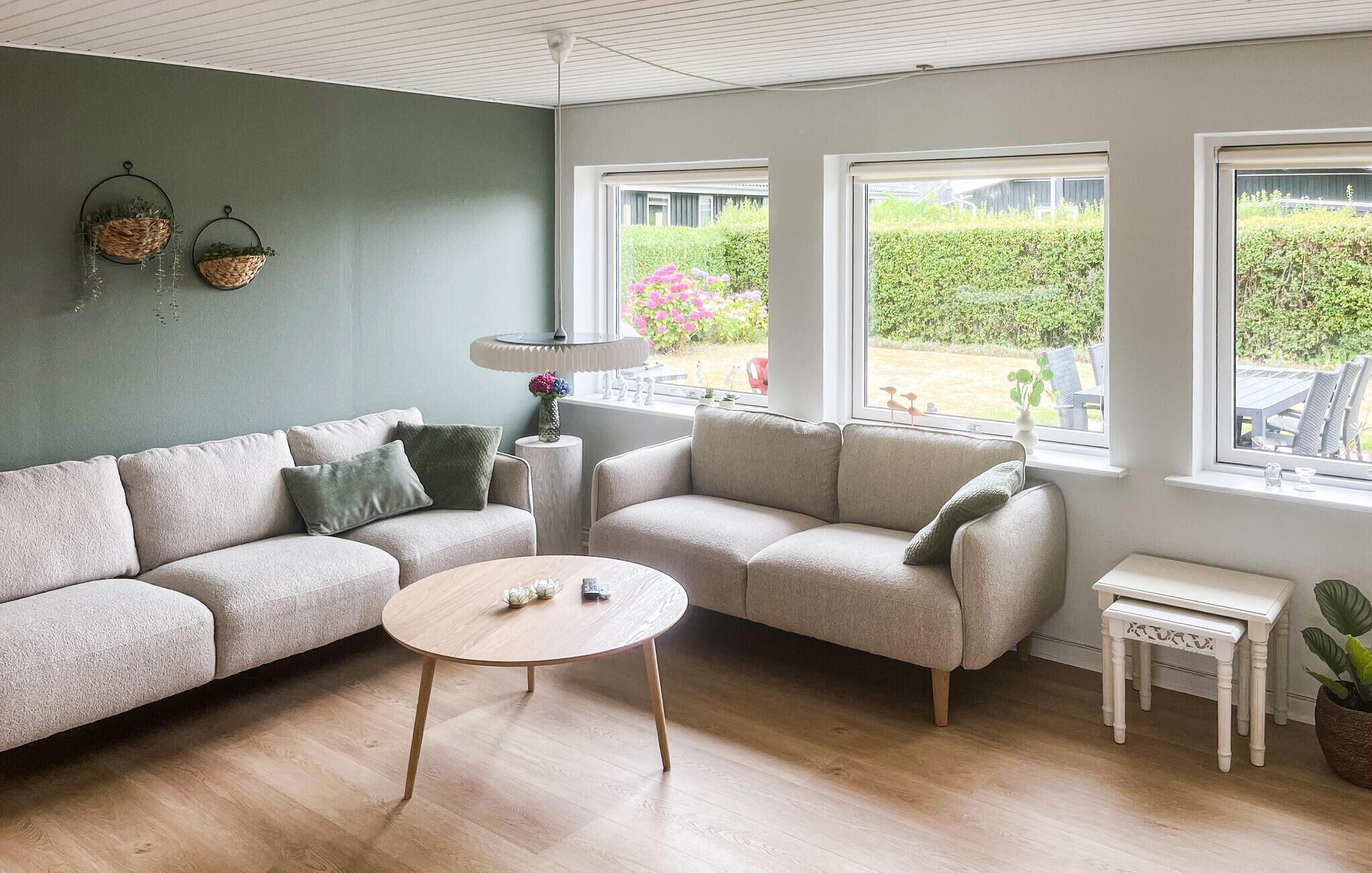 Ein Wohnzimmer mit einer Couch, einem Couchtisch und zwei Fenstern mit Blick ins Freie.