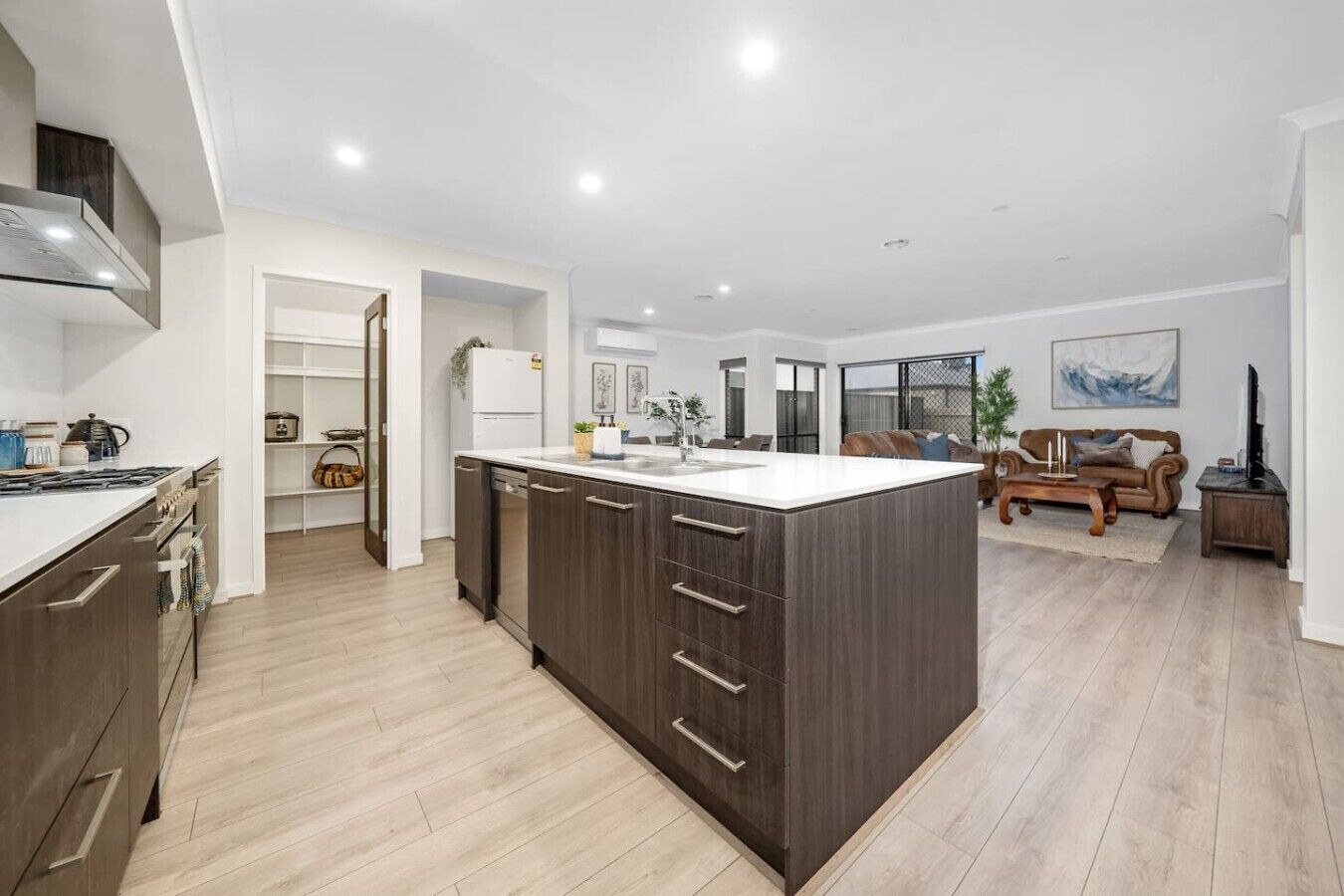 A modern kitchen with a central island, wooden cabinetry, and a dining area with a sofa and coffee table.