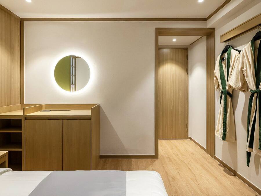 Une chambre d’hôtel moderne équipée d’un lit, d’une armoire en bois, d’un miroir rond et d’un porte-peignoir.