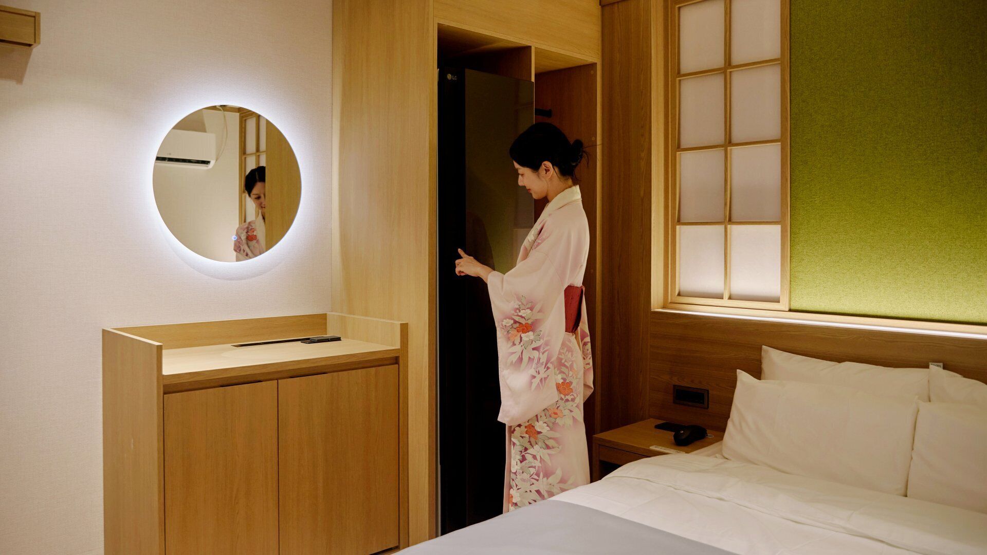 Una habitación de hotel con una cama, una mesita de noche con teléfono, un espejo y un armario de madera.