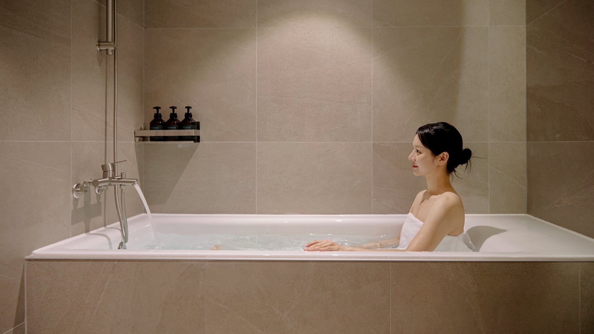Una mujer en una bañera con cabezal de ducha y grifo.