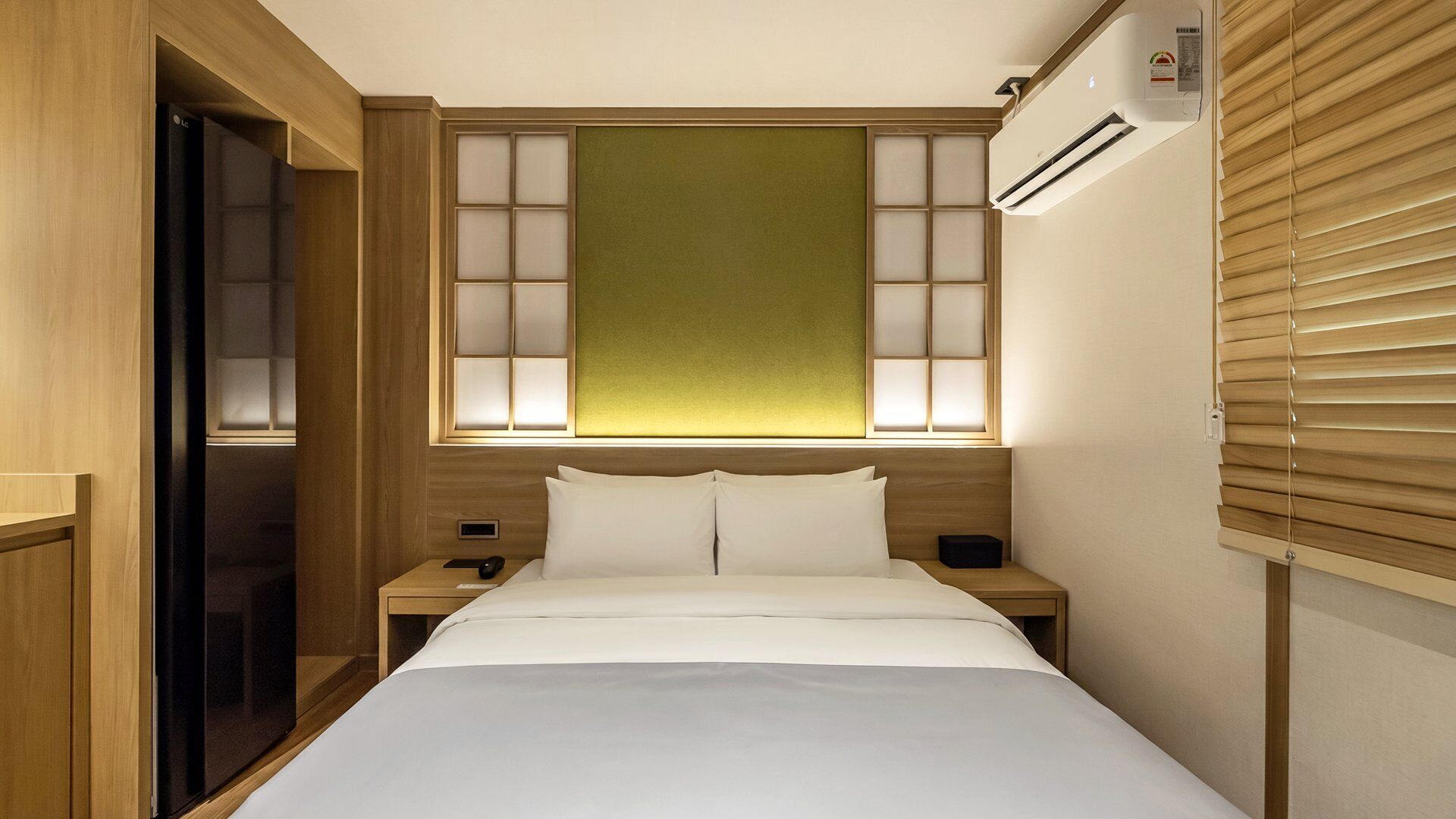 A hotel room with a bed, bedside tables, a wardrobe, and an air conditioning unit.