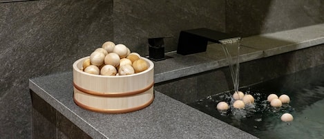 Un cuenco de madera lleno de objetos redondos sobre una repisa de piedra junto a una fuente.