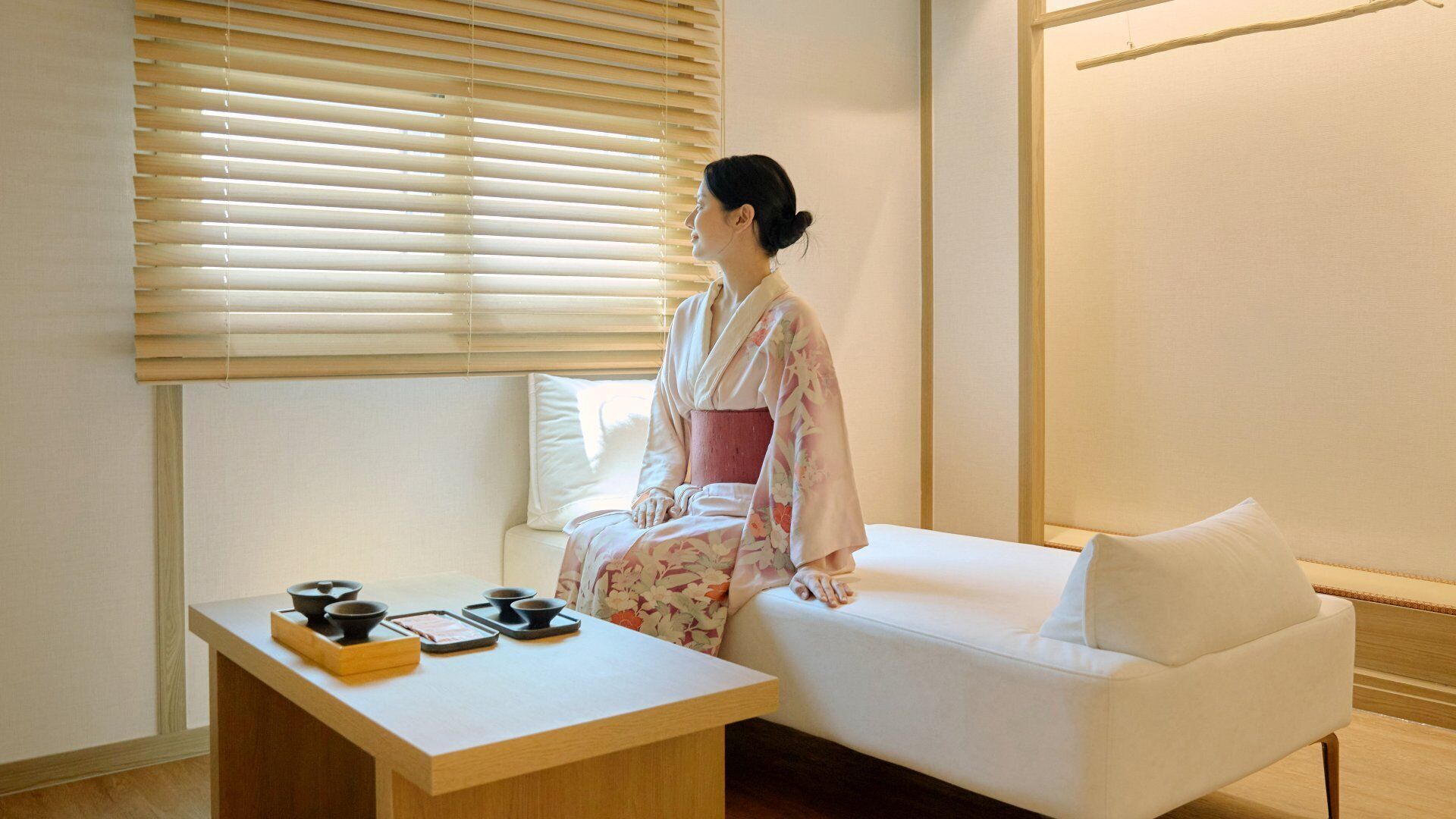 A room with a white sofa, a wooden table with black bowls, and a window with wooden blinds.