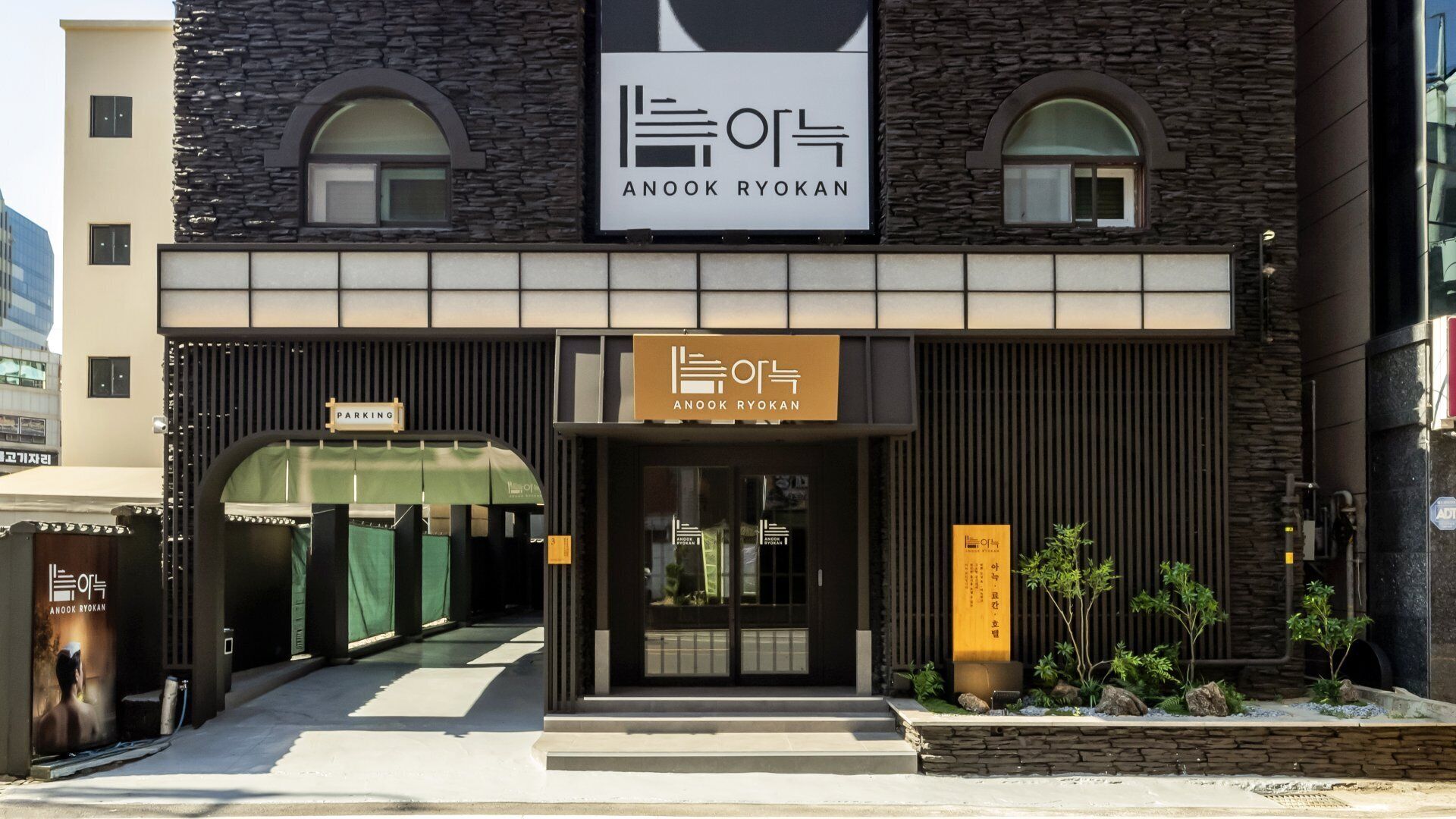Un edificio con fachada de piedra, un letrero que dice 'ANOOK RYOKAN' y un cartel de estacionamiento.