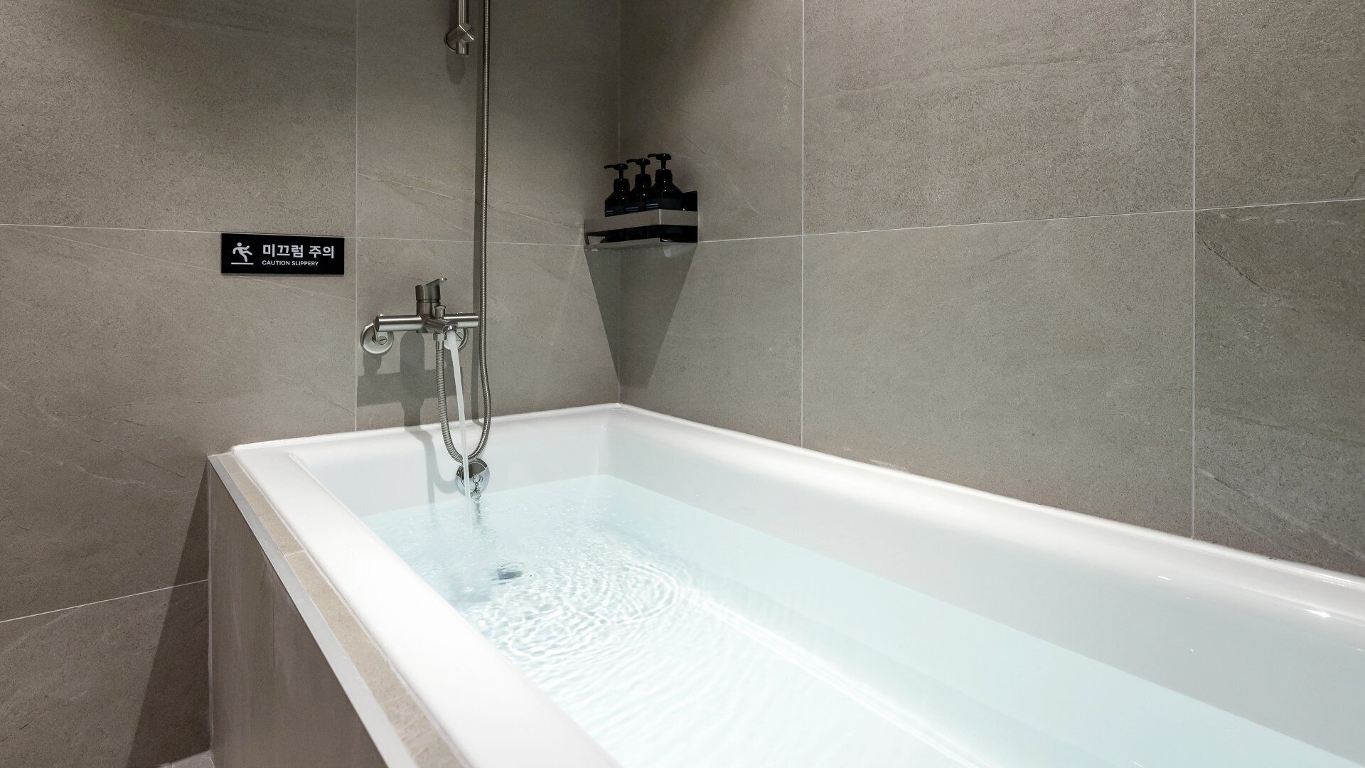 Une salle de bain moderne avec une baignoire, une douche et un distributeur de savon liquide placé sur une étagère.