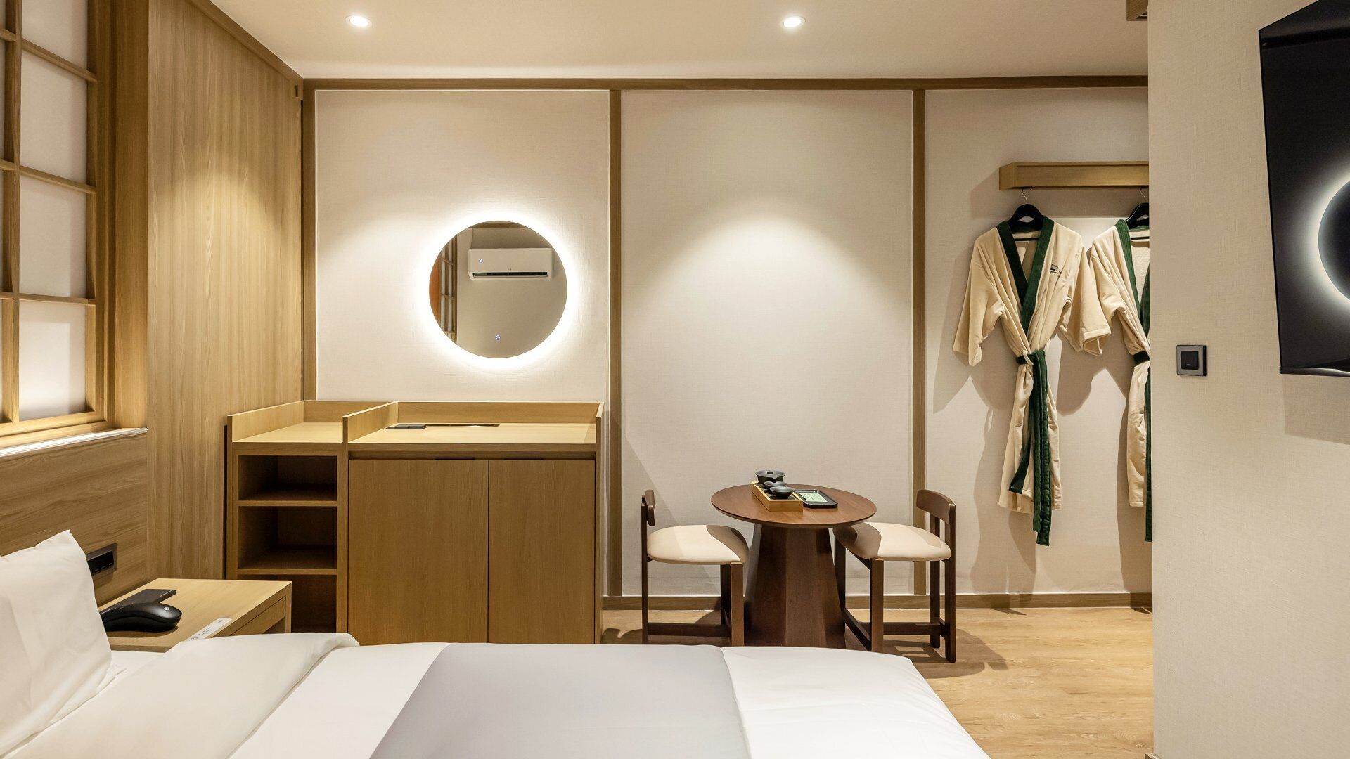 A hotel room with a bed, a desk, a chair, a round mirror, and a coat rack.