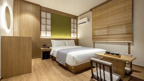 Habitación de hotel con cama, mesita de noche, escritorio, silla y ventana con persianas.