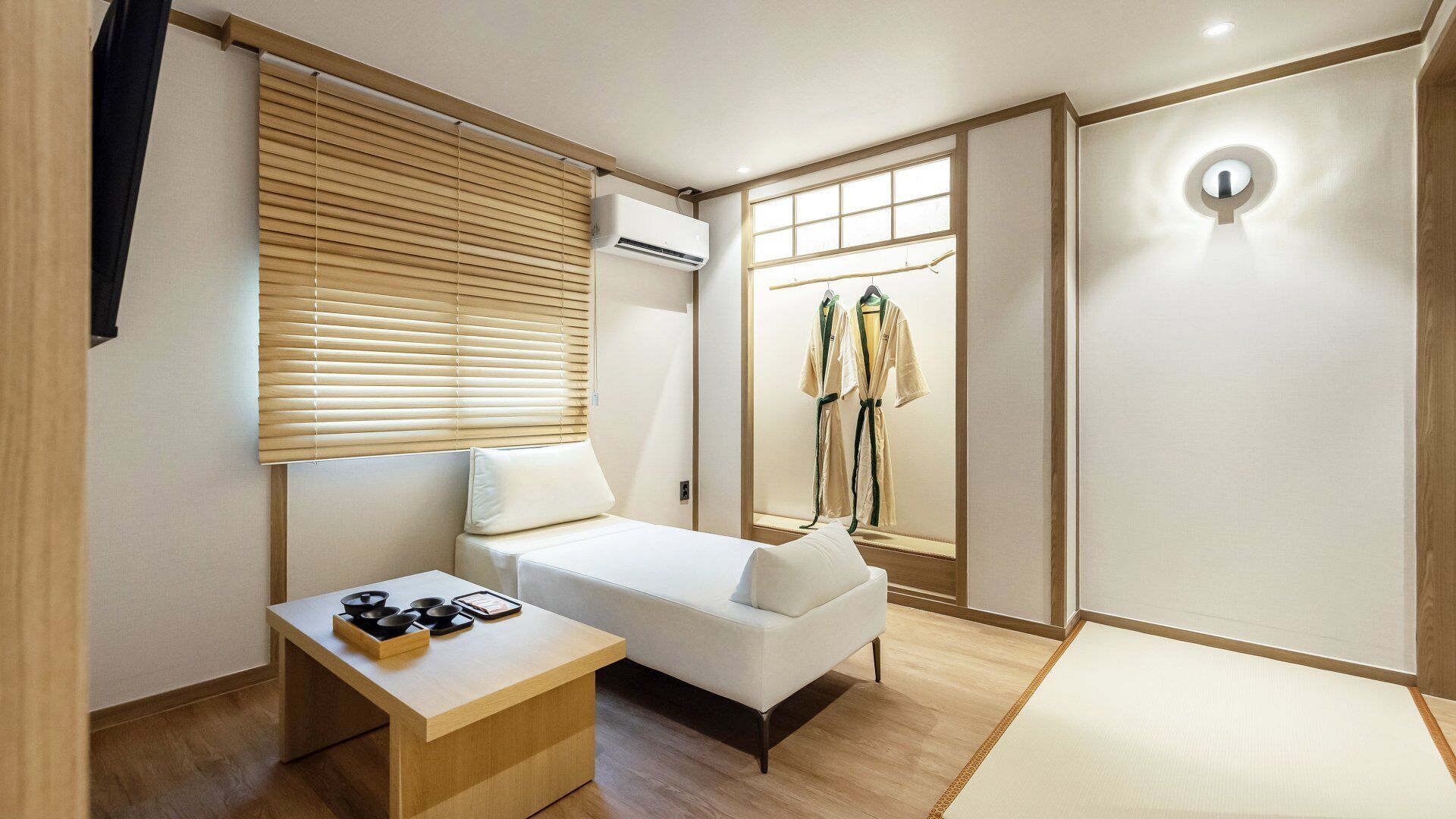A modern hotel room with a bed, bedside table, and a window with blinds.