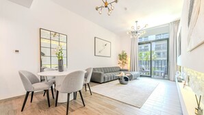 En moderne stue med spiseplads, en grå sofa, et rundt sofabord og en balkon med udsigt.