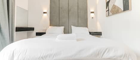 A modern hotel room with a large bed, two bedside tables, a headboard, and a wall-mounted artwork.