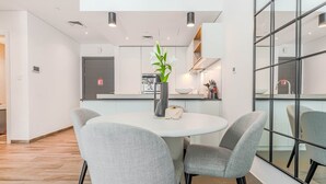 Et moderne køkken med en central ø, et spiseområde med et rundt bord og fire stole, samt et stort vindue med kig til køkkenet.