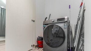 Et lille, moderne vaskerum med en frontbetjent vaskemaskine, en rød balje og et metalstativ til tørring.
