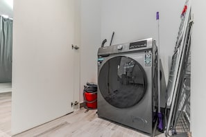 Ein kompakter, moderner Waschraum mit einer Waschmaschine, einem roten Eimer und einem Metalltrockner.