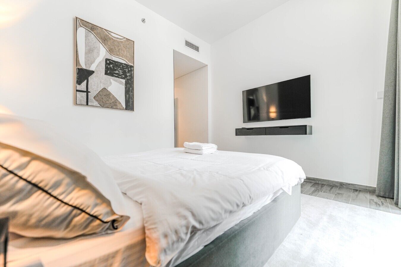 Ein modernes Schlafzimmer mit einem Bett, einem Flachbildfernseher an der Wand und einem Gemälde über dem Bett.