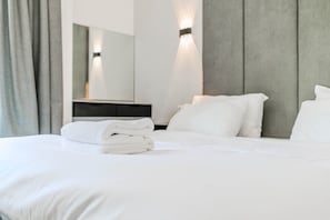 A hotel room with a neatly made bed, a large mirror, and a modern light fixture.