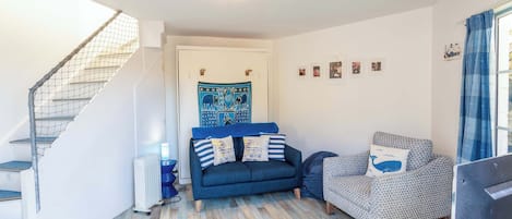 A living room with a staircase, a blue sofa, patterned armchairs, and a wall with framed pictures.