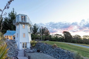A two-story house with a balcony, a stone pathway leading to the entrance, and a grassy area with trees. - The Lighthouse at Ligar Bay - Romantic Coastal Escape with Spa (Ligar Bay)