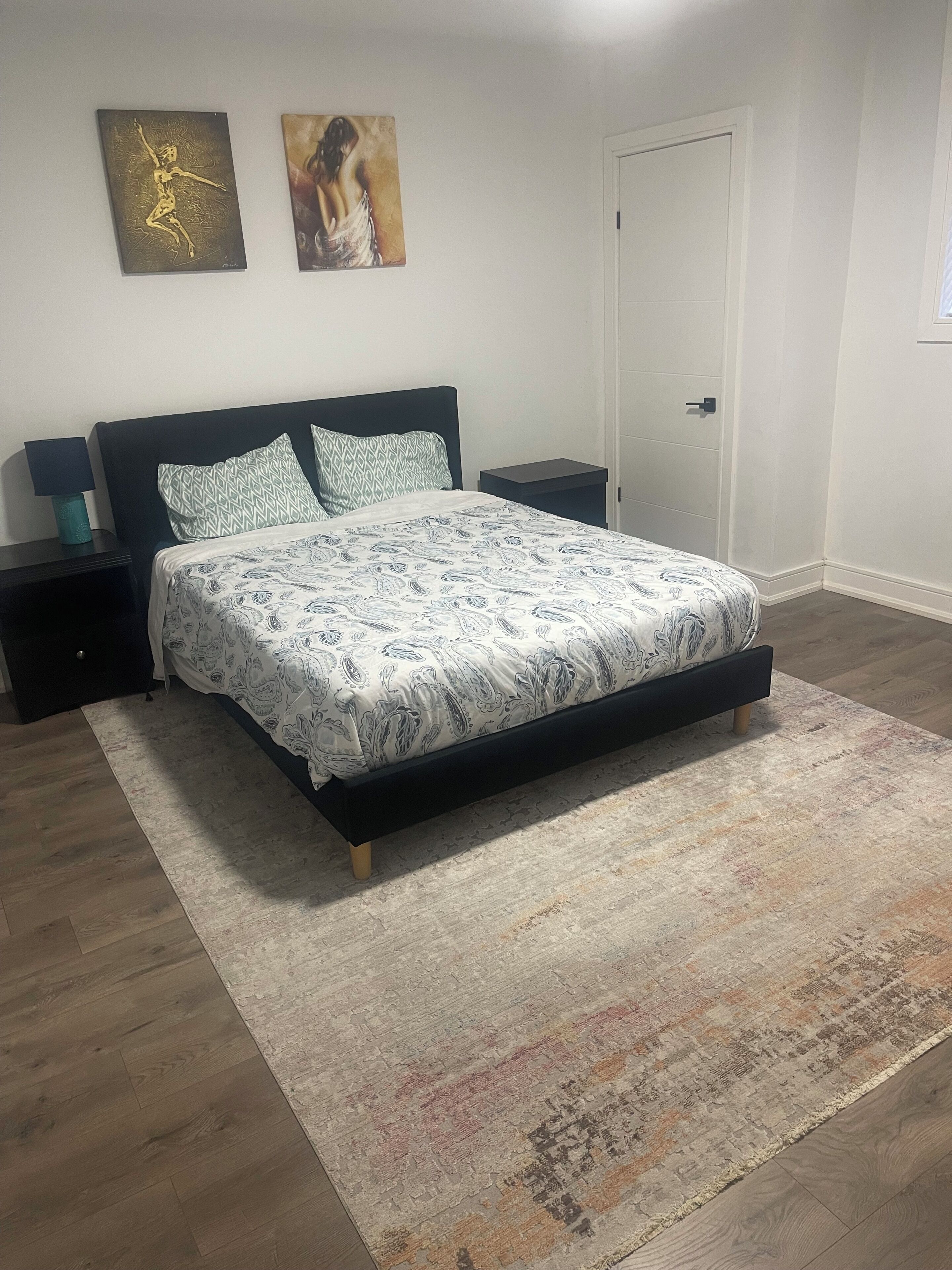 A bedroom with a bed, nightstands, a rug, and two wall art pieces.