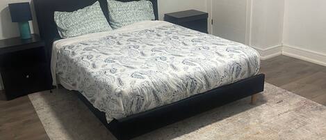A bedroom with a bed, nightstands, a rug, and two wall art pieces.