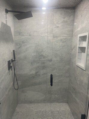 A shower stall with a handheld showerhead, a wall-mounted control panel, and a tiled floor. - Private spacious bedroom with ensuite and living space (Oshawa)