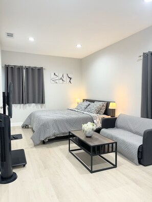 Un dormitorio moderno con cama, sofá, mesa de centro, televisor y lámpara.